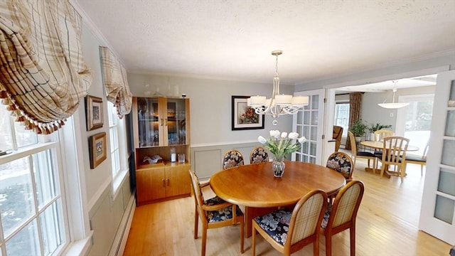 dining space with a notable chandelier, ornamental molding, a textured ceiling, and light wood-type flooring