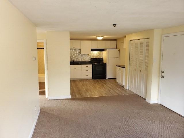 kitchen featuring carpet flooring, white cabinetry, backsplash, white fridge, and black range