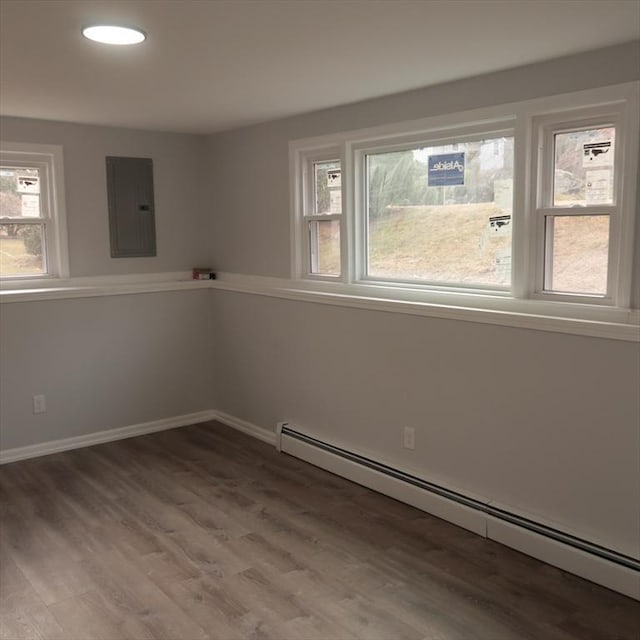 empty room with wood-type flooring, electric panel, and a baseboard heating unit