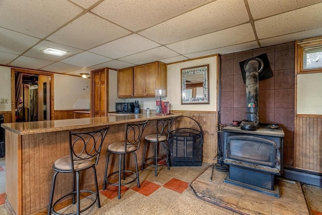 kitchen featuring a paneled ceiling, wainscoting, brown cabinetry, and light floors