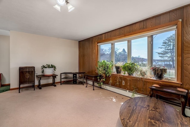 living area featuring carpet, wood walls, a baseboard heating unit, baseboards, and ceiling fan