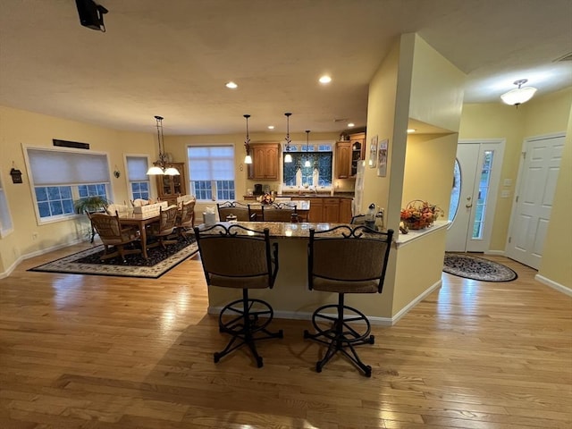 kitchen with dark stone countertops, kitchen peninsula, a notable chandelier, light wood-type flooring, and a breakfast bar