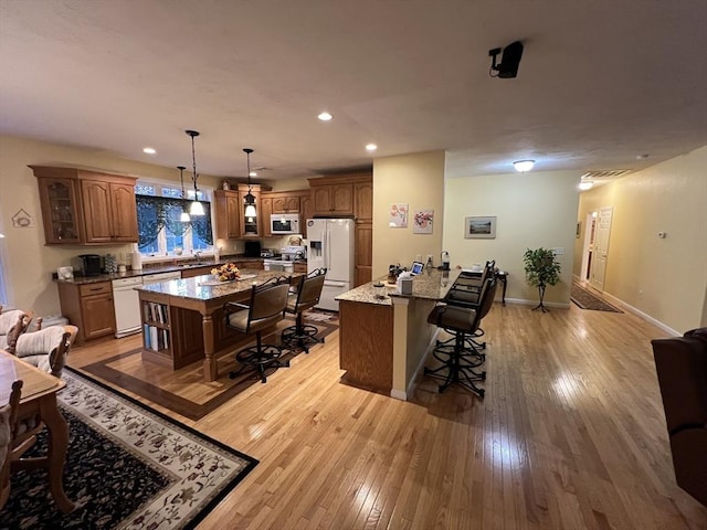 interior space featuring light hardwood / wood-style floors, a breakfast bar area, decorative light fixtures, white appliances, and light stone countertops