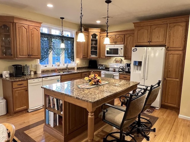 kitchen featuring white appliances, a center island, decorative light fixtures, dark stone countertops, and sink