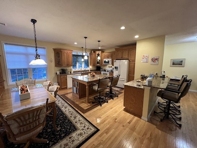 kitchen with a kitchen bar, white appliances, a kitchen island, light hardwood / wood-style flooring, and light stone counters