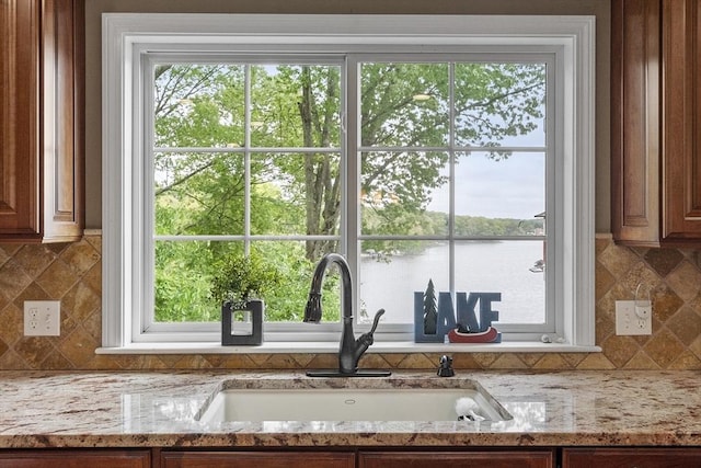 4 Elizabeth Rd, Hudson, MA 01749 - kitchen view of a sink, backsplash, a nearby body of water, light stone countertops, and brown cabinetry