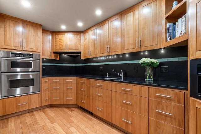 kitchen with double oven, a sink, dark countertops, and light wood-type flooring