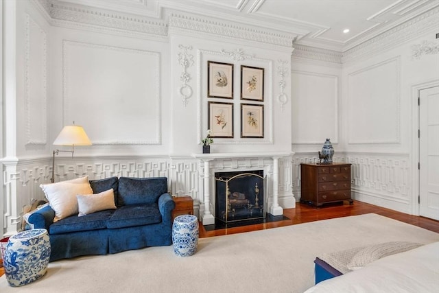 living area featuring a fireplace with flush hearth, ornamental molding, a decorative wall, and wood finished floors