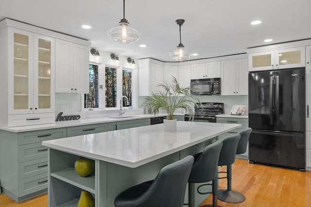 kitchen with light wood-type flooring, sink, black appliances, decorative light fixtures, and a kitchen island