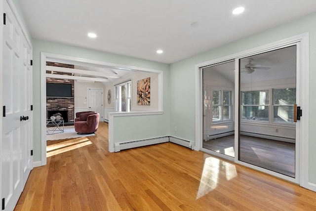 interior space with ceiling fan, a baseboard radiator, light hardwood / wood-style flooring, beamed ceiling, and a fireplace