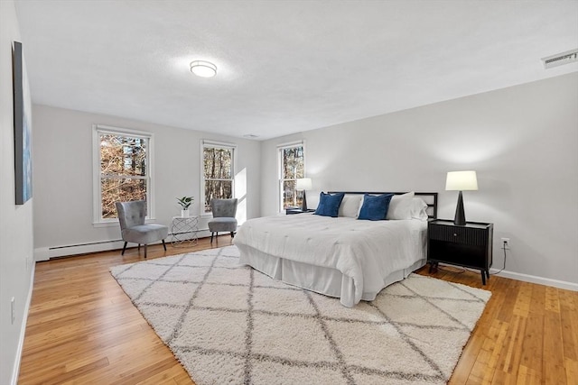 bedroom with wood-type flooring, baseboard heating, and multiple windows