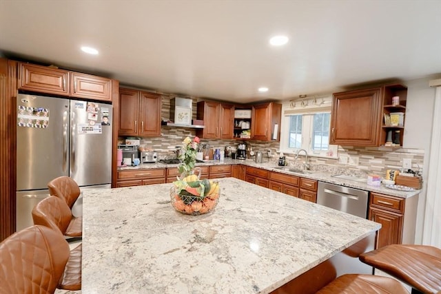 kitchen featuring a breakfast bar area, stainless steel appliances, wall chimney range hood, light stone counters, and sink