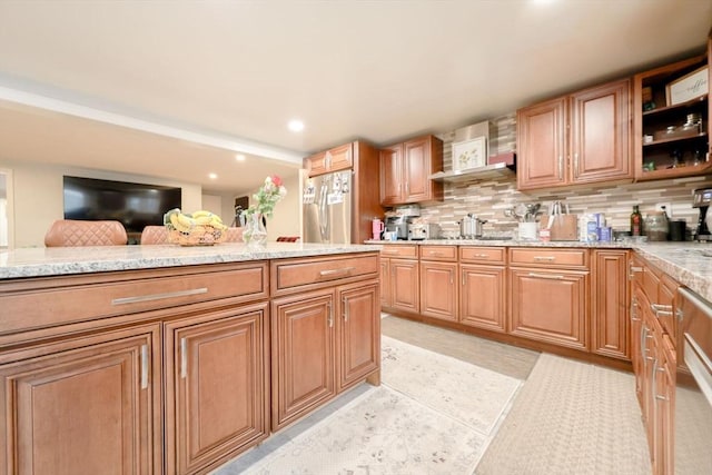 kitchen featuring light stone countertops, decorative backsplash, and stainless steel refrigerator