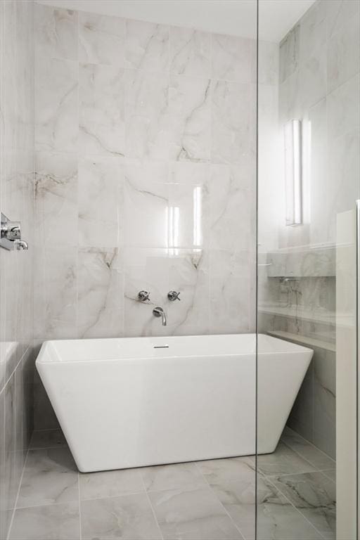 bathroom with marble finish floor, a soaking tub, and tile walls