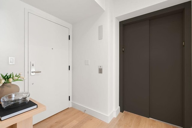 foyer entrance with light wood-type flooring, baseboards, and elevator