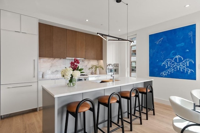 kitchen featuring paneled built in fridge, a sink, light wood-style flooring, modern cabinets, and light countertops