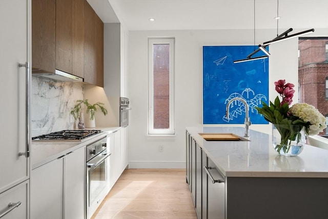 kitchen featuring light wood finished floors, backsplash, modern cabinets, a sink, and appliances with stainless steel finishes