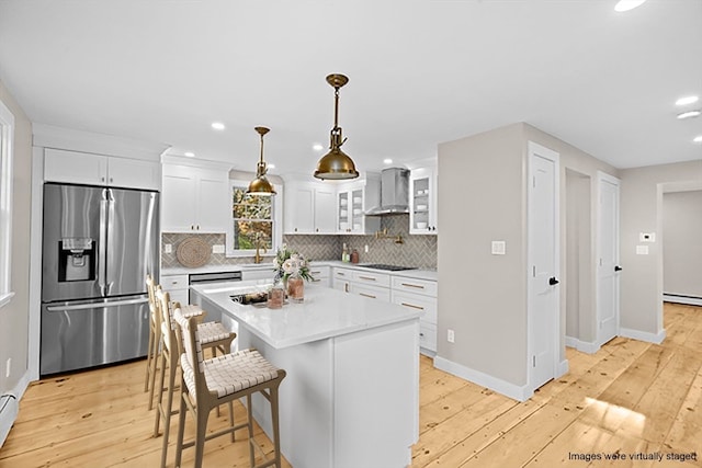 kitchen featuring white cabinetry, a kitchen island, wall chimney exhaust hood, light wood-type flooring, and stainless steel fridge