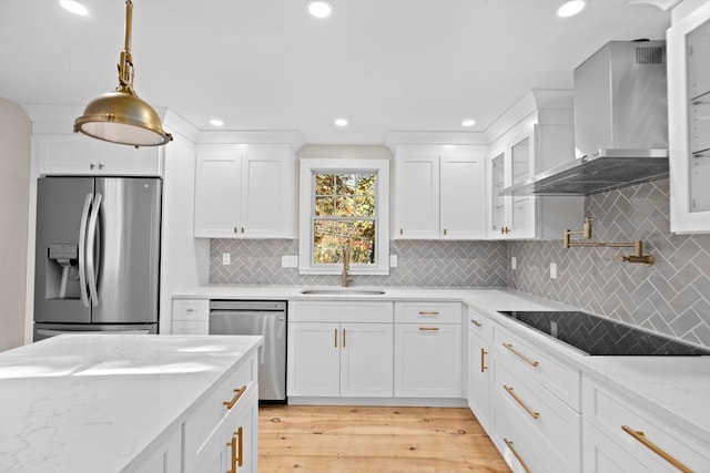 kitchen featuring white cabinetry, appliances with stainless steel finishes, wall chimney range hood, light wood-type flooring, and light stone counters