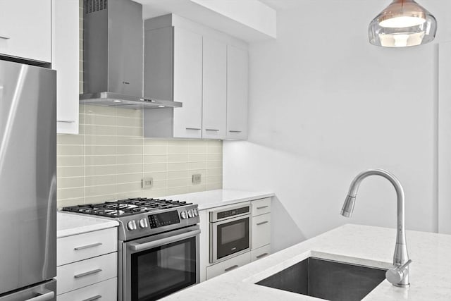 kitchen featuring white cabinetry, wall chimney range hood, sink, stainless steel appliances, and light stone counters