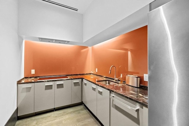 kitchen featuring light hardwood / wood-style flooring, stainless steel fridge, dishwasher, sink, and dark stone counters