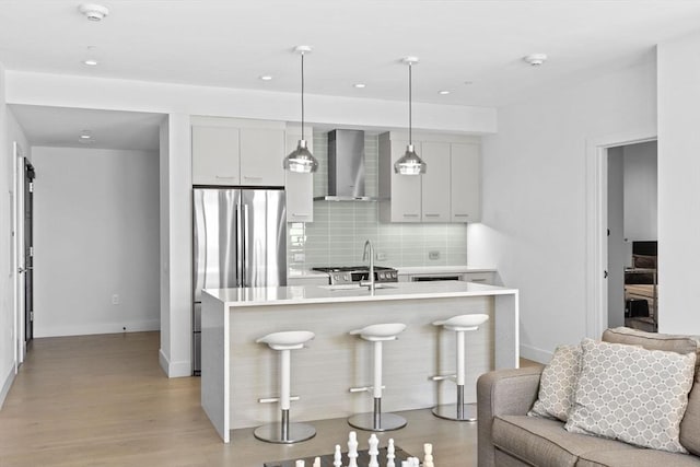 kitchen featuring a kitchen breakfast bar, decorative light fixtures, backsplash, a center island with sink, and wall chimney exhaust hood