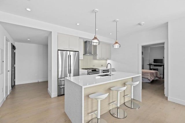 kitchen with appliances with stainless steel finishes, wall chimney range hood, an island with sink, decorative backsplash, and sink