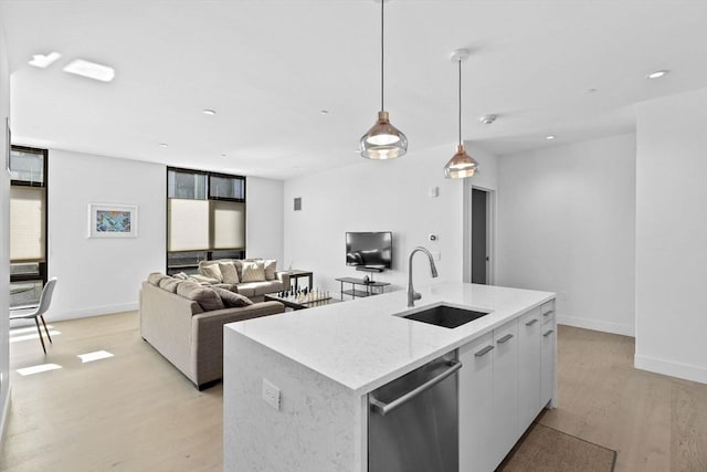 kitchen with stainless steel dishwasher, sink, white cabinets, pendant lighting, and an island with sink