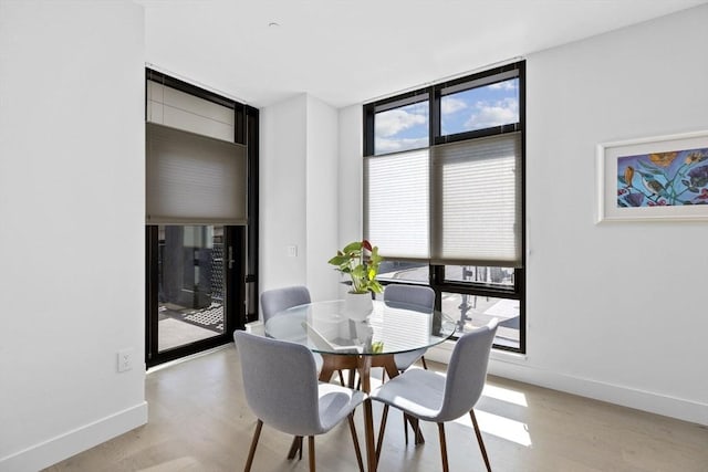 dining area with light wood-type flooring, expansive windows, and a healthy amount of sunlight