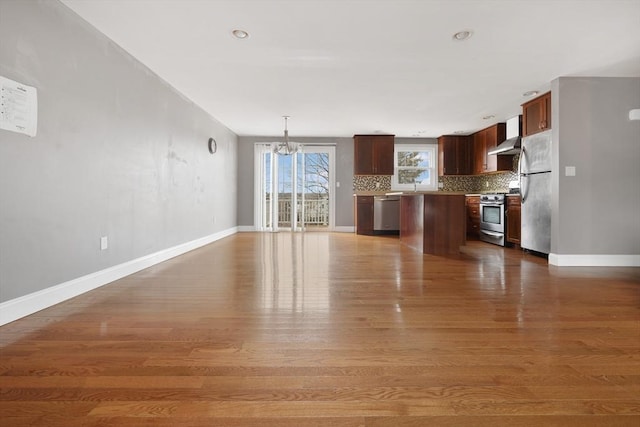 kitchen featuring open floor plan, stainless steel appliances, hanging light fixtures, and light countertops