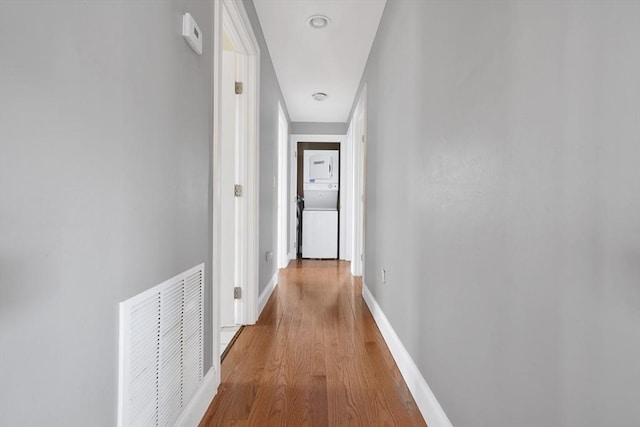 hallway featuring light wood-style floors, baseboards, visible vents, and stacked washing maching and dryer