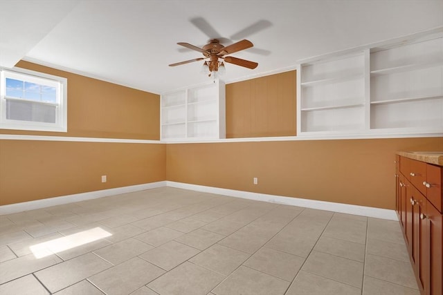 spare room featuring built in shelves, ceiling fan, baseboards, and light tile patterned floors