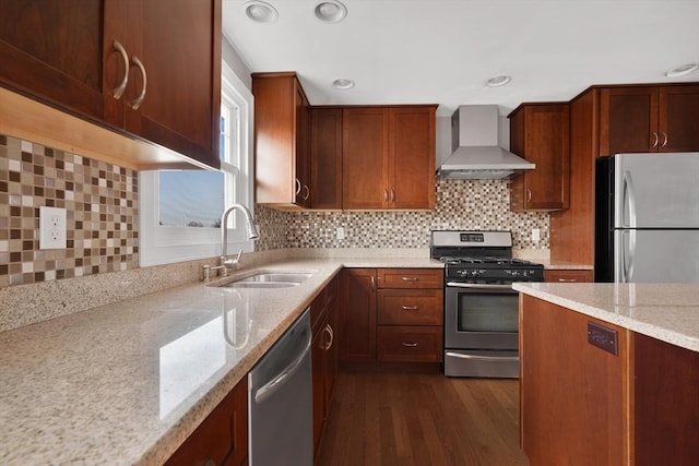 kitchen featuring light stone counters, wall chimney range hood, a sink, and appliances with stainless steel finishes