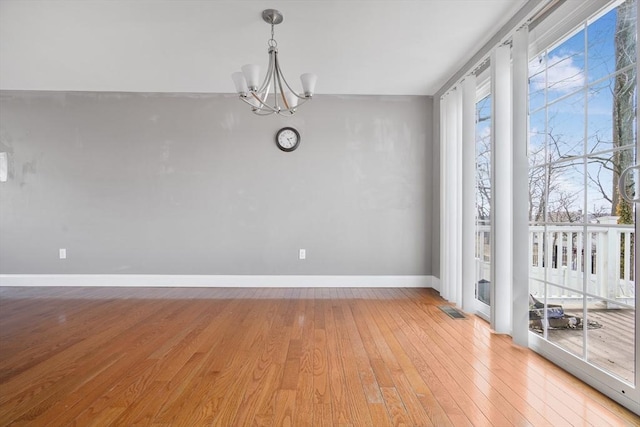 unfurnished dining area featuring baseboards, visible vents, light wood-style flooring, and a notable chandelier