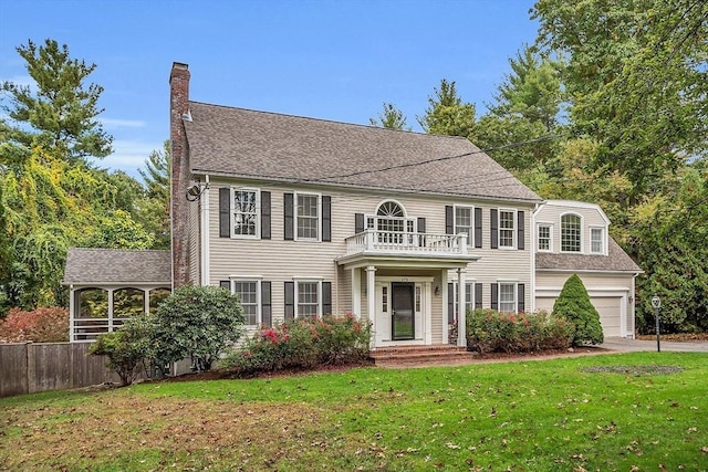 colonial house with a balcony, a garage, and a front lawn