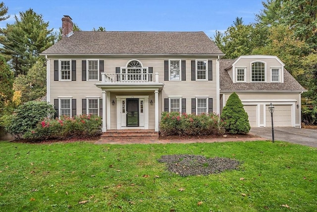 colonial inspired home with a balcony, a garage, and a front lawn