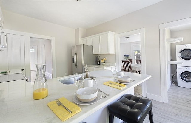 29 Maple St Unit 2, Uxbridge, MA 01569 - kitchen with estacked washer and dryer, stainless steel fridge, a breakfast bar area, white cabinetry, and light wood-style flooring