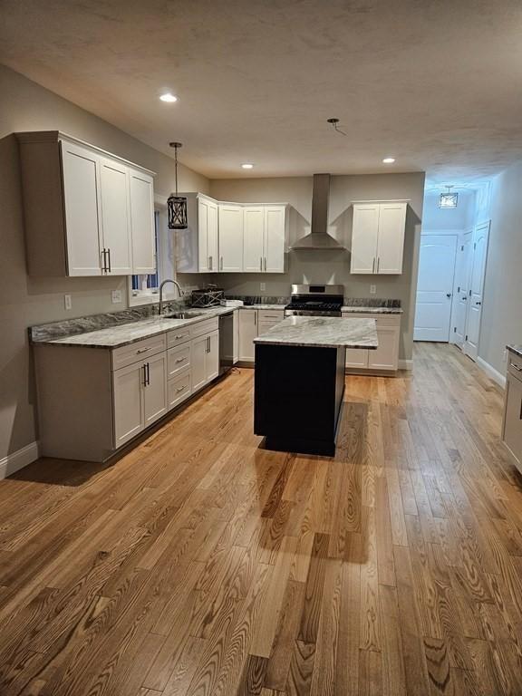 kitchen featuring stainless steel appliances, decorative light fixtures, wall chimney exhaust hood, light hardwood / wood-style flooring, and a center island