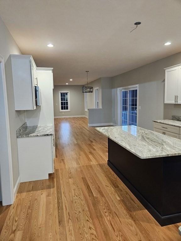 kitchen with light hardwood / wood-style floors, light stone counters, white cabinetry, and a center island