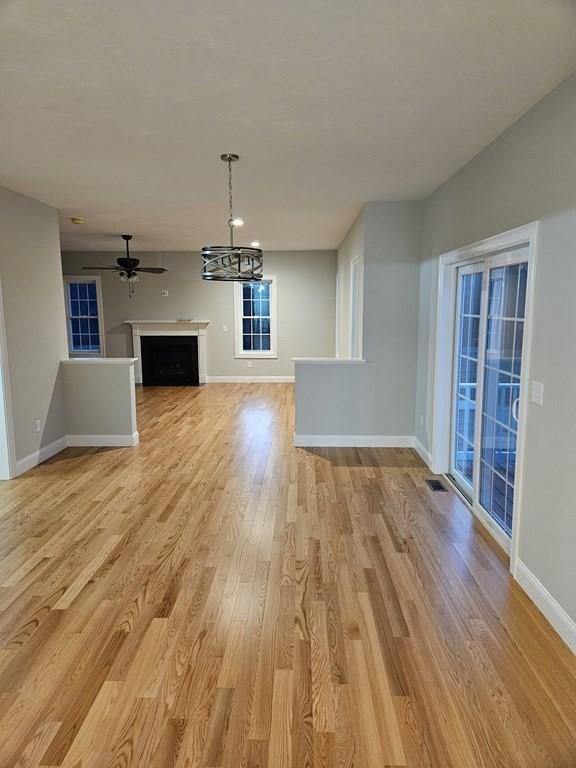 unfurnished living room with ceiling fan with notable chandelier and light hardwood / wood-style floors