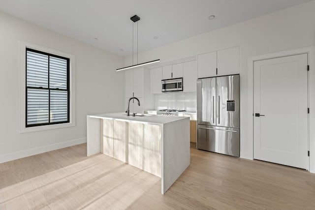 kitchen featuring an island with sink, sink, white cabinets, hanging light fixtures, and stainless steel appliances