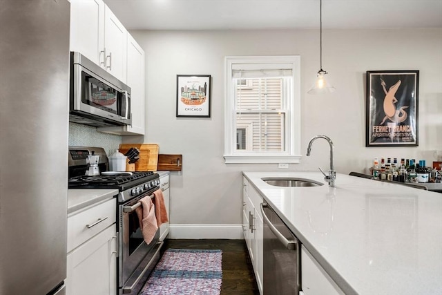 kitchen featuring stainless steel appliances, dark wood-type flooring, a sink, white cabinets, and baseboards