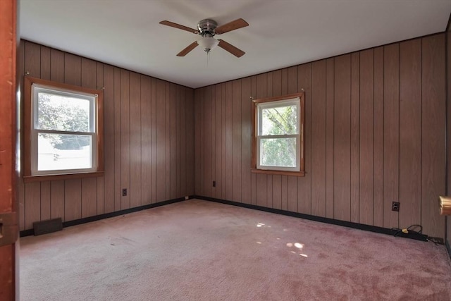 carpeted empty room with wood walls, plenty of natural light, and ceiling fan