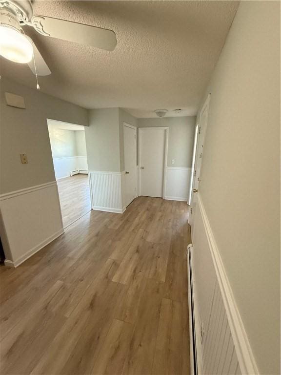 hallway with baseboard heating, a textured ceiling, and light wood-type flooring