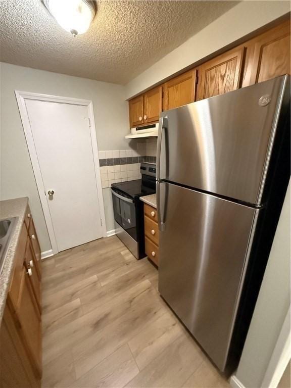 kitchen featuring tasteful backsplash, stainless steel appliances, a textured ceiling, and light wood-type flooring