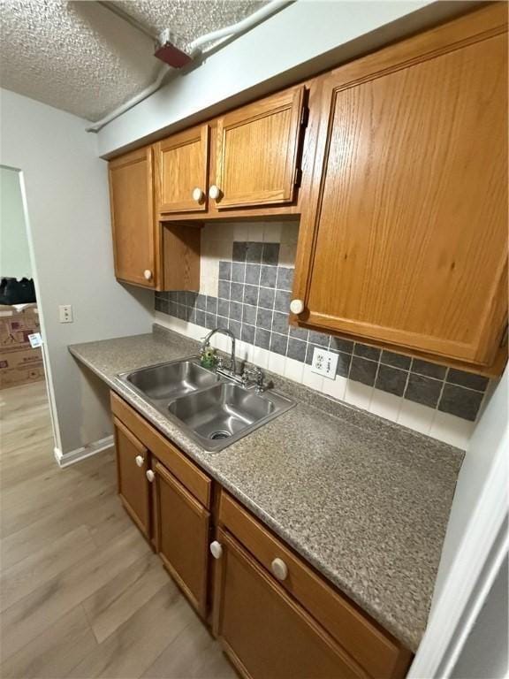 kitchen with a textured ceiling, sink, decorative backsplash, and light hardwood / wood-style flooring