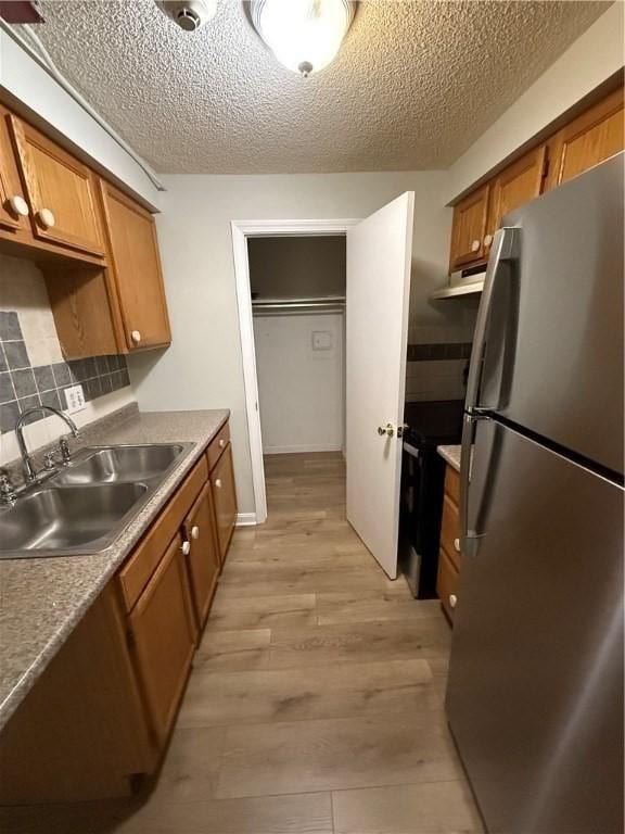 kitchen with sink, black electric range, a textured ceiling, light wood-type flooring, and stainless steel fridge