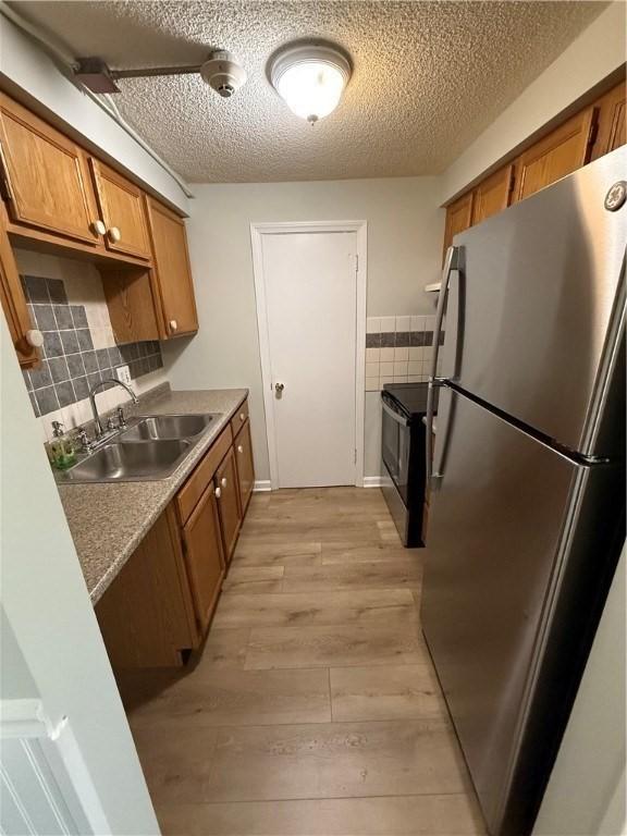 kitchen with stainless steel refrigerator, sink, light wood-type flooring, electric range, and a textured ceiling