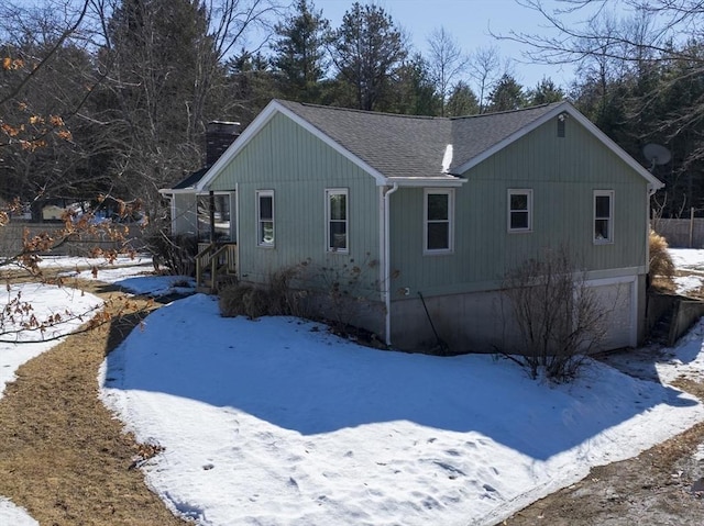 snow covered property featuring a garage, a chimney, and roof with shingles