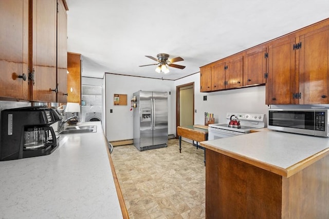 kitchen with washer / clothes dryer, light countertops, appliances with stainless steel finishes, brown cabinetry, and a sink